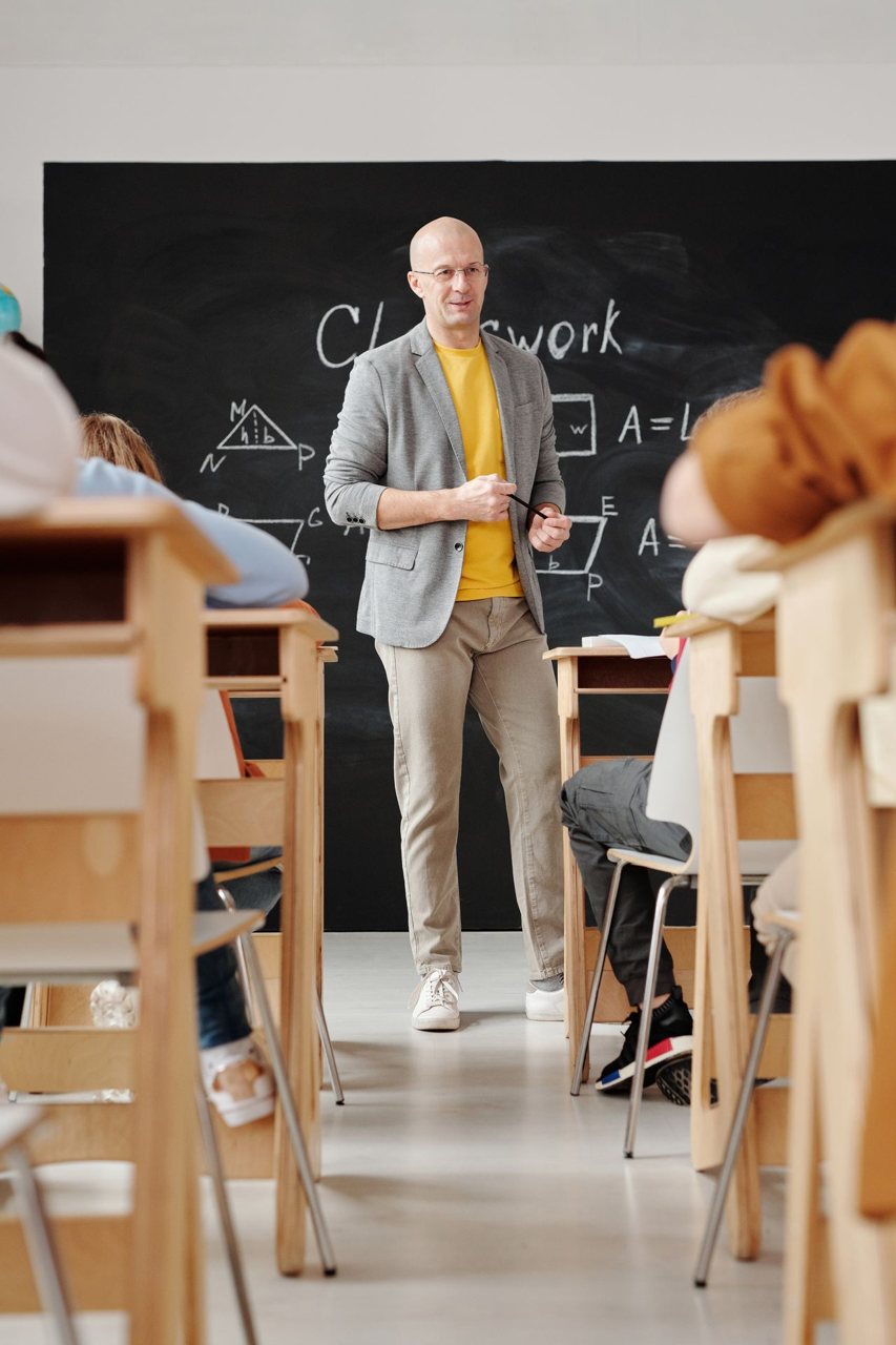 Free Bald teacher explaining geometry on blackboard to attentive students in classroom. Stock Photo